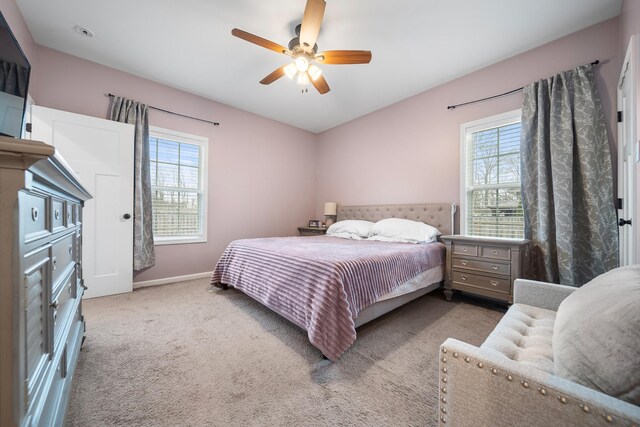 bedroom featuring light carpet, ceiling fan, multiple windows, and baseboards