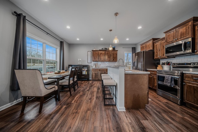 kitchen with stainless steel appliances, an island with sink, dark wood finished floors, and decorative light fixtures