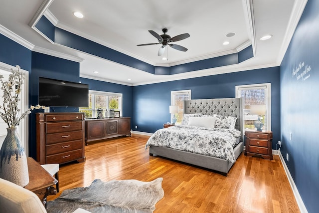 bedroom featuring baseboards, a raised ceiling, ceiling fan, ornamental molding, and light wood-style floors