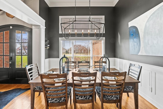 dining room with french doors, a wainscoted wall, ornamental molding, wood finished floors, and a chandelier