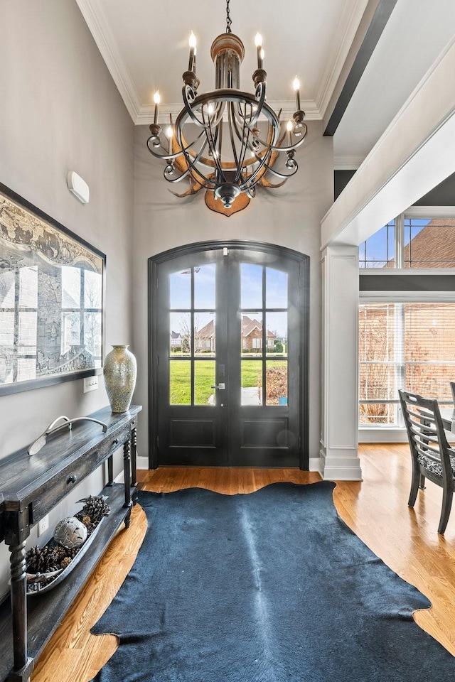 entryway with an inviting chandelier, ornamental molding, wood finished floors, and french doors