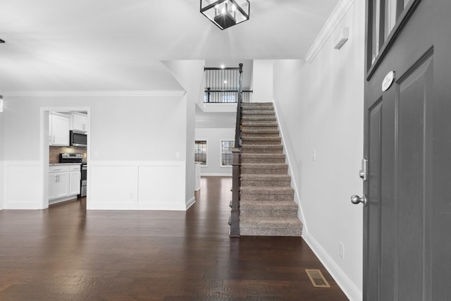 entrance foyer with a wainscoted wall, visible vents, ornamental molding, stairway, and dark wood-style floors