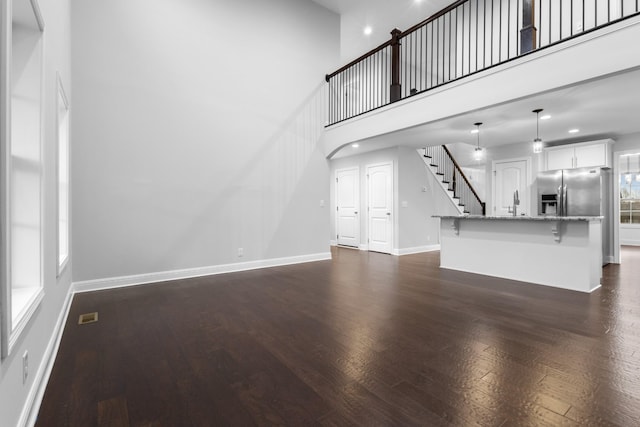 unfurnished living room with a high ceiling, visible vents, baseboards, stairway, and dark wood-style floors