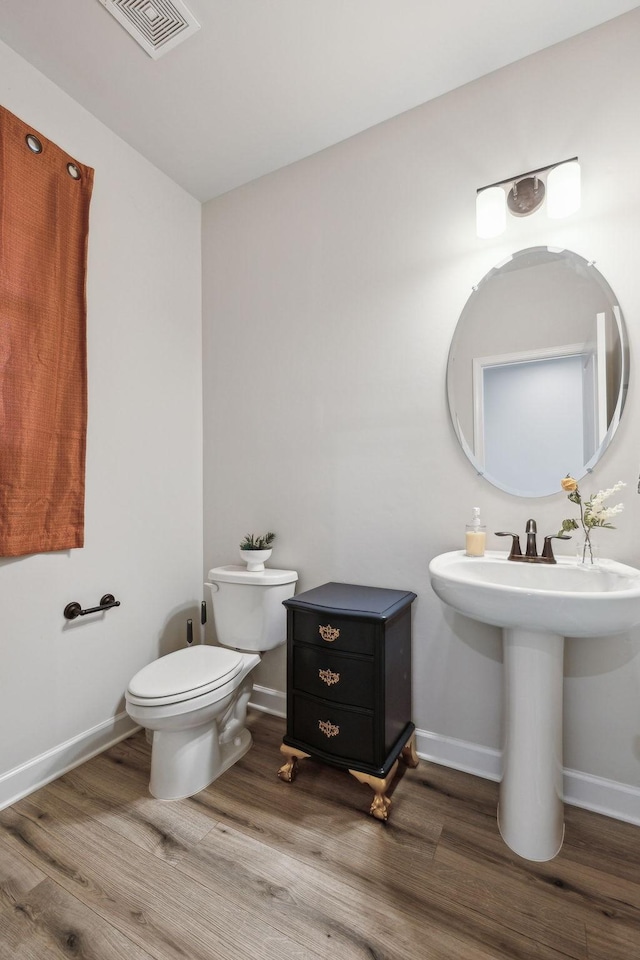 bathroom featuring toilet, a sink, wood finished floors, visible vents, and baseboards