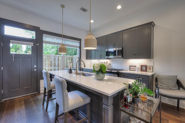 kitchen with a sink, light countertops, decorative backsplash, appliances with stainless steel finishes, and dark wood-style flooring