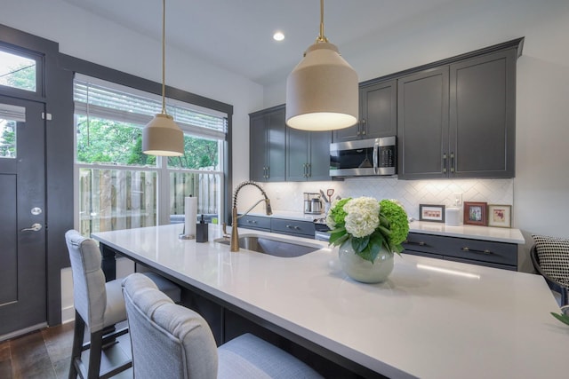 kitchen featuring a sink, stainless steel microwave, decorative backsplash, and light countertops