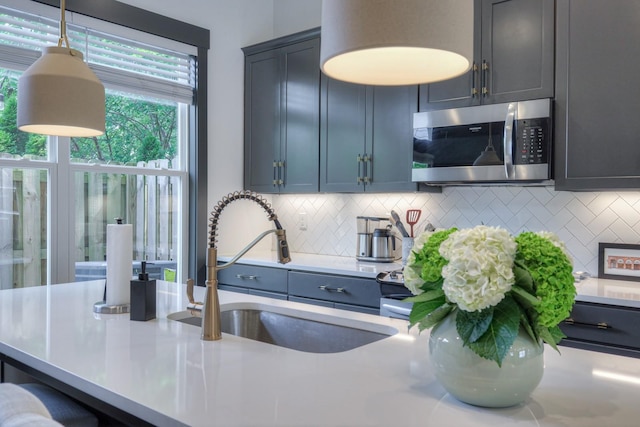 kitchen with stainless steel microwave, light countertops, decorative backsplash, hanging light fixtures, and a sink