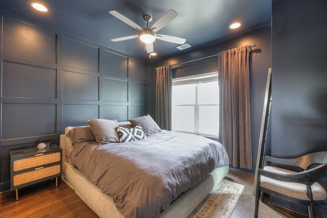 bedroom with a ceiling fan, wood finished floors, visible vents, crown molding, and a decorative wall