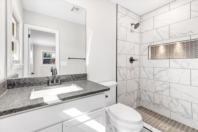 bathroom with toilet, visible vents, tiled shower, and vanity