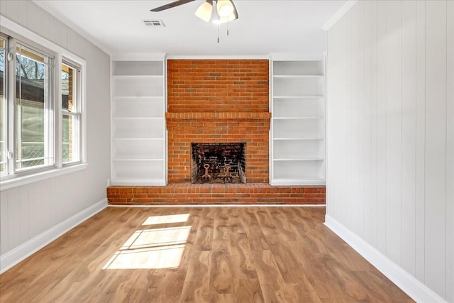 unfurnished living room featuring built in shelves, a brick fireplace, wood finished floors, and visible vents