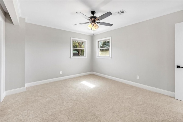 empty room featuring light colored carpet, visible vents, ornamental molding, ceiling fan, and baseboards