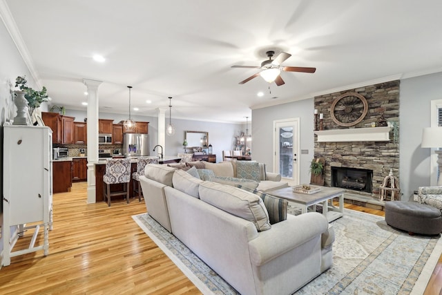 living area featuring a stone fireplace, recessed lighting, a ceiling fan, light wood-style floors, and ornamental molding