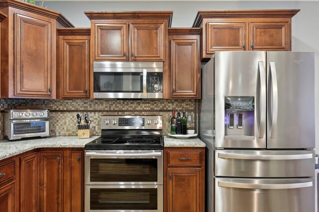 kitchen featuring a toaster, appliances with stainless steel finishes, light stone countertops, tasteful backsplash, and brown cabinetry