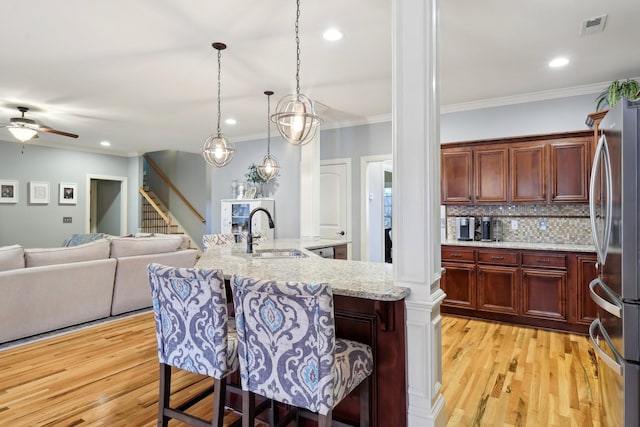 kitchen featuring visible vents, hanging light fixtures, freestanding refrigerator, a sink, and a kitchen bar