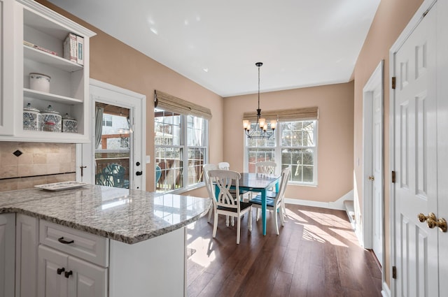 kitchen with tasteful backsplash, dark wood finished floors, decorative light fixtures, light stone countertops, and white cabinetry