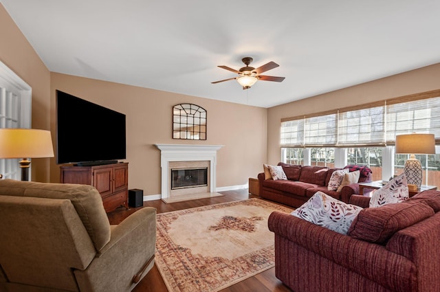 living room with a fireplace with flush hearth, a ceiling fan, baseboards, and dark wood-style floors