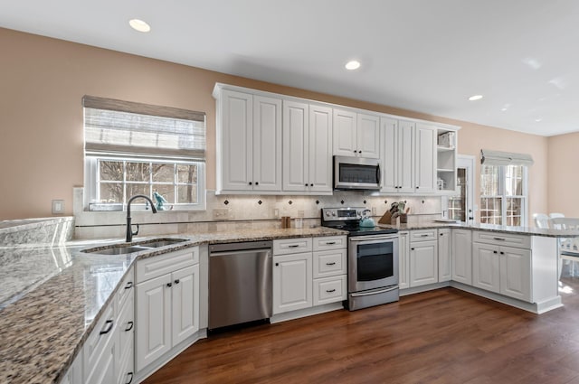 kitchen with stainless steel appliances, a peninsula, a sink, white cabinets, and light stone countertops