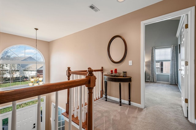 hallway featuring baseboards, an upstairs landing, visible vents, and light colored carpet