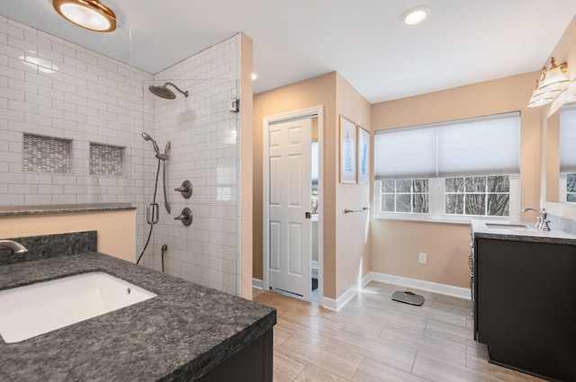 full bathroom with tiled shower, two vanities, a sink, and baseboards