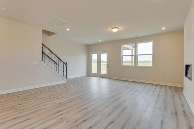 unfurnished living room featuring stairs, visible vents, light wood-style flooring, and baseboards