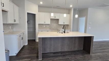 kitchen with a sink, white cabinets, dark wood-style floors, tasteful backsplash, and an island with sink