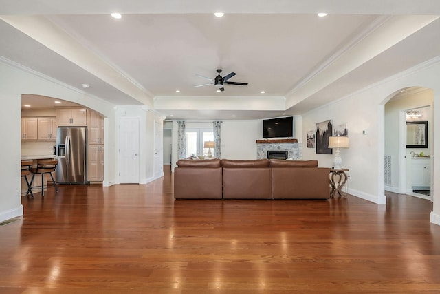 living room with arched walkways, a tray ceiling, a glass covered fireplace, and dark wood finished floors