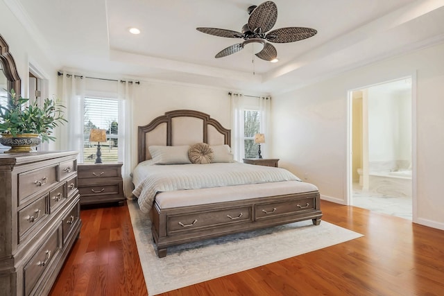 bedroom with a tray ceiling, dark wood-style flooring, baseboards, and ensuite bathroom