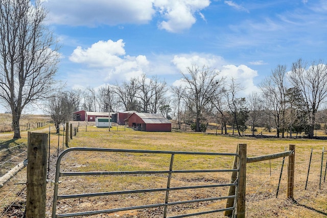 view of gate with a rural view, fence, an outdoor structure, and a lawn