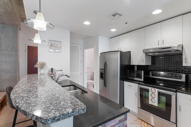 kitchen featuring under cabinet range hood, a sink, white cabinets, appliances with stainless steel finishes, and decorative light fixtures