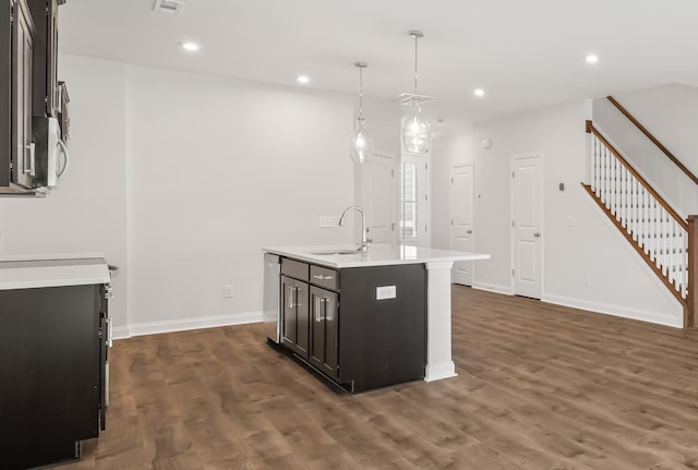 kitchen featuring decorative light fixtures, dark wood-type flooring, a sink, light countertops, and a center island with sink