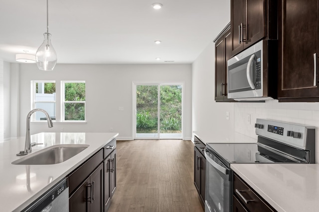 kitchen featuring a sink, light countertops, appliances with stainless steel finishes, backsplash, and pendant lighting