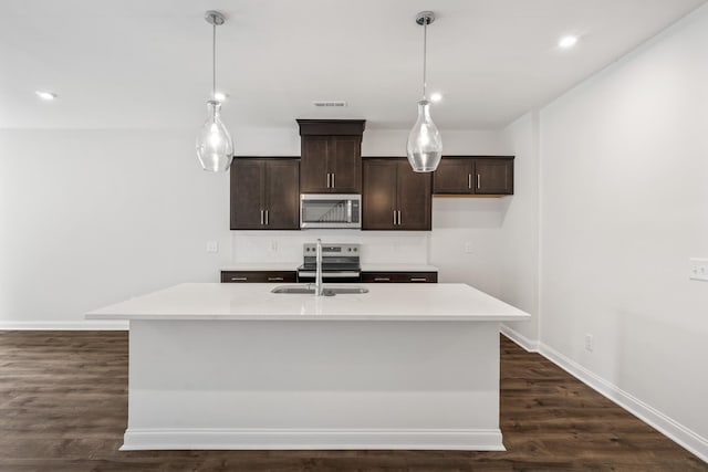 kitchen featuring stainless steel appliances, light countertops, a center island with sink, and decorative light fixtures