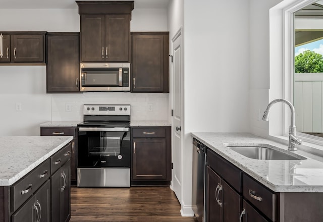 kitchen with dark wood finished floors, appliances with stainless steel finishes, light stone countertops, dark brown cabinets, and a sink