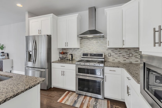 kitchen with appliances with stainless steel finishes, white cabinets, wall chimney range hood, and dark stone countertops