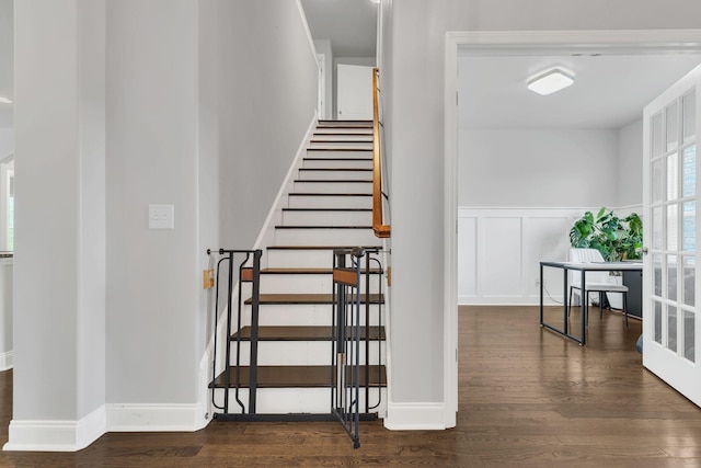 staircase featuring a decorative wall, wood finished floors, and wainscoting