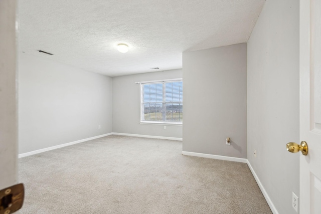 spare room featuring carpet, visible vents, a textured ceiling, and baseboards