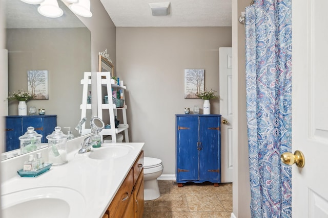 bathroom featuring a sink, a textured ceiling, toilet, and double vanity