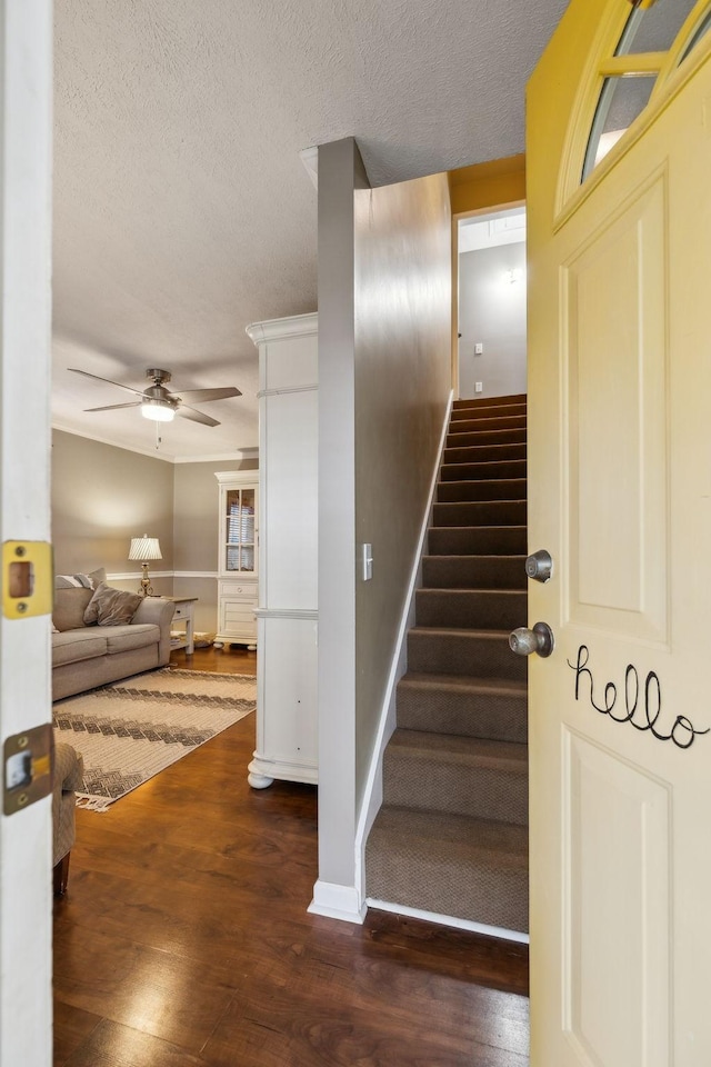 stairway featuring a ceiling fan, a textured ceiling, baseboards, and wood finished floors