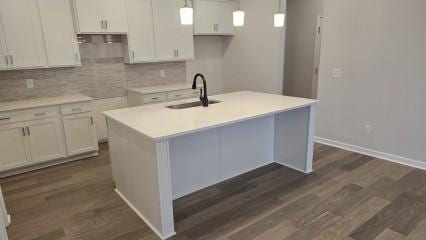 kitchen with a center island with sink, light countertops, a sink, and decorative light fixtures