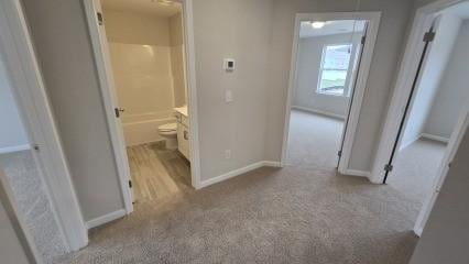 hallway featuring light carpet and baseboards