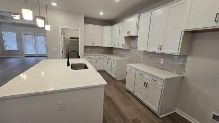 kitchen featuring white cabinets, a kitchen island with sink, light countertops, and a sink