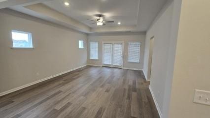 unfurnished room with ceiling fan, a tray ceiling, dark wood-type flooring, and baseboards