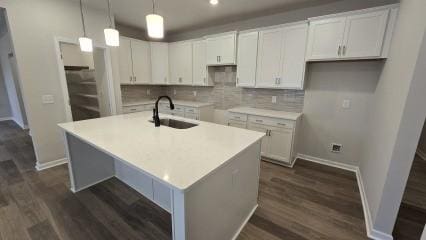 kitchen with a kitchen island with sink, white cabinetry, light countertops, and a sink