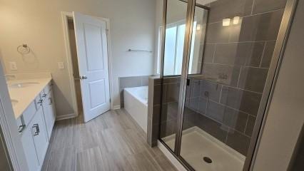 bathroom with a garden tub, a shower stall, wood finished floors, and vanity