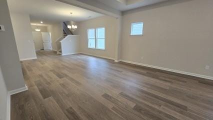 unfurnished living room with dark wood-style floors, a chandelier, stairway, and baseboards