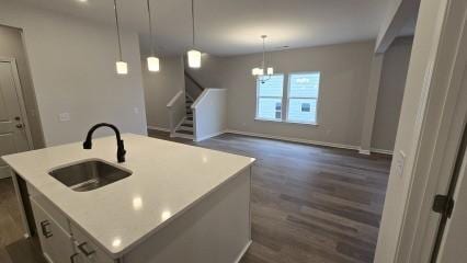 kitchen featuring dark wood-type flooring, a sink, hanging light fixtures, and an island with sink