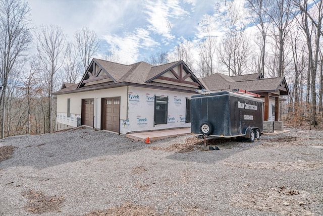 view of front of property with an attached garage, a shingled roof, gravel driveway, and stucco siding