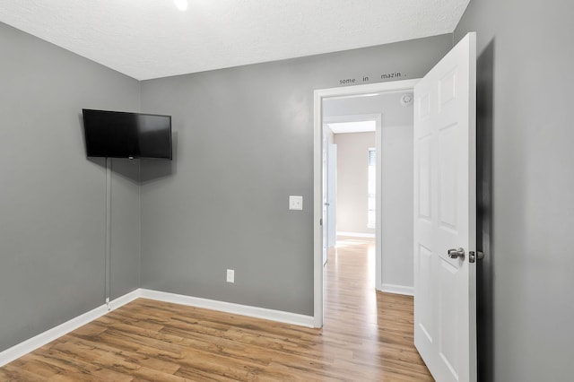 unfurnished bedroom with light wood-type flooring, baseboards, and a textured ceiling