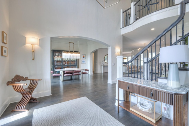 entryway featuring arched walkways, dark wood-style flooring, stairway, a high ceiling, and baseboards