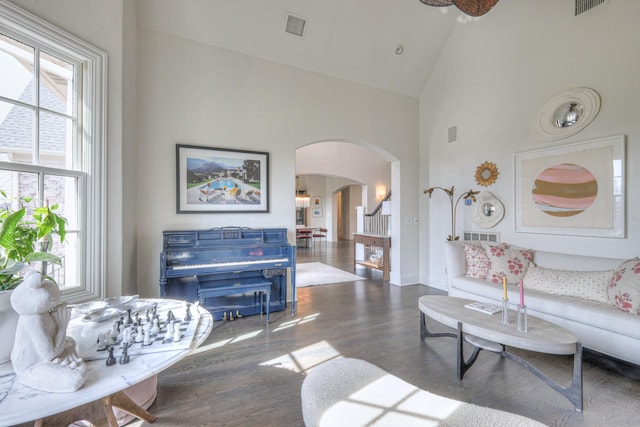 living room featuring arched walkways, dark wood-style flooring, visible vents, high vaulted ceiling, and baseboards